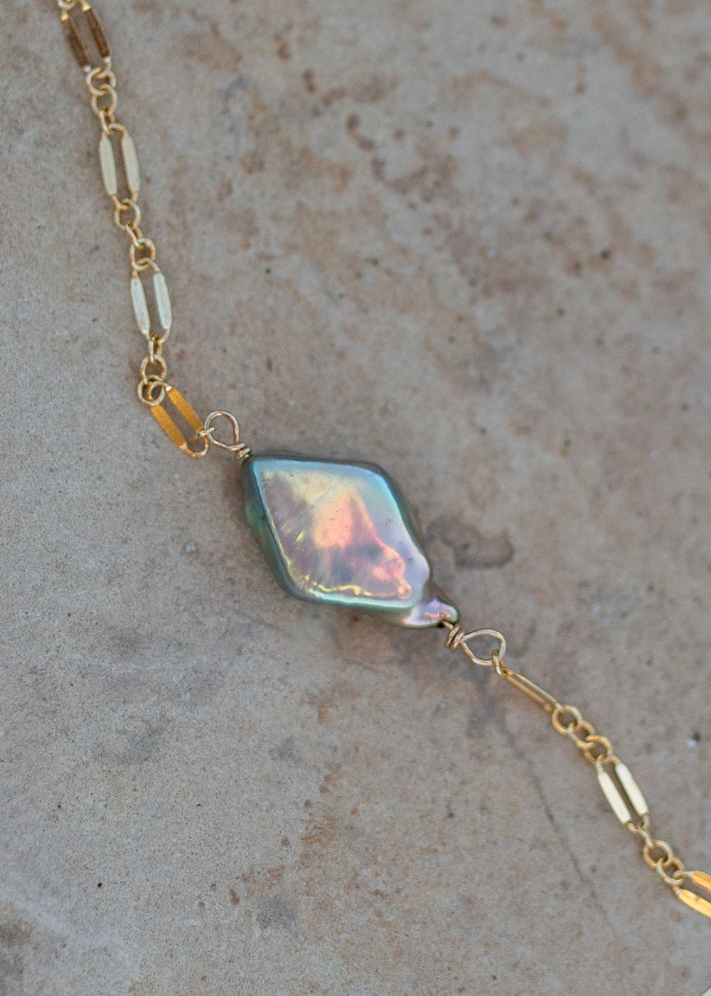 Sparkly gold necklace with a diamond shaped sage green pearl in the middle