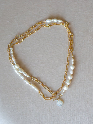 Two-layered necklaces with gold chain and pearl beads on a beige background