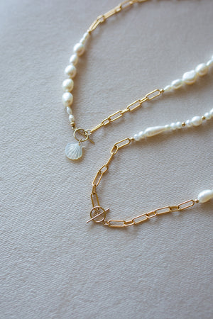 Gold chain necklace with pearl beads on a soft beige background. One necklace has a mother of pearl scallop charm, one is plain.