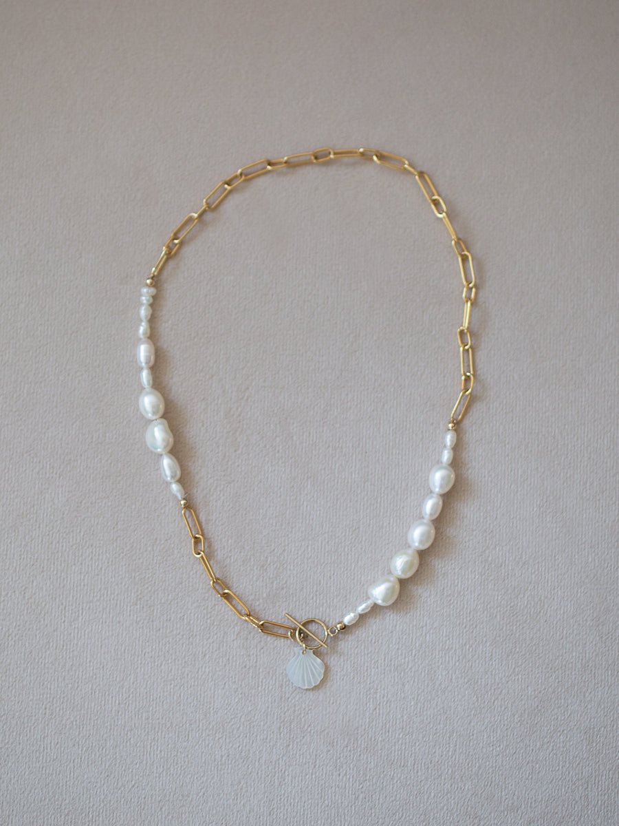Gold chain necklace with pearl beads and carved pearl seashell charm on a soft beige background
