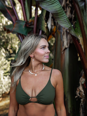 Woman wearing a green swimsuit with a pearl and gold necklace, in a tropical setting