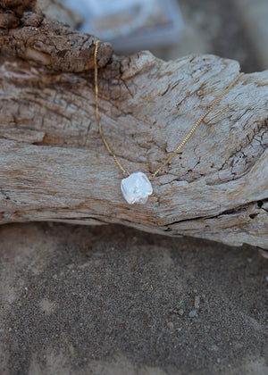 A necklace of white keishi pearl with gold venetian box chain, draped ver a piece of driftwood