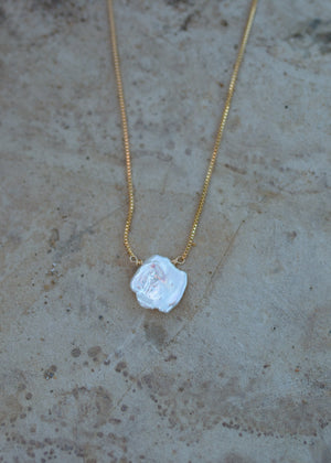Dainty gold box chain with a large white keishi pearl pendant and a sandstone background