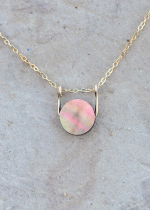 An up close view of the mother of pearl coin pendant, strung with a gold sliding bail on a dainty gold cable chain