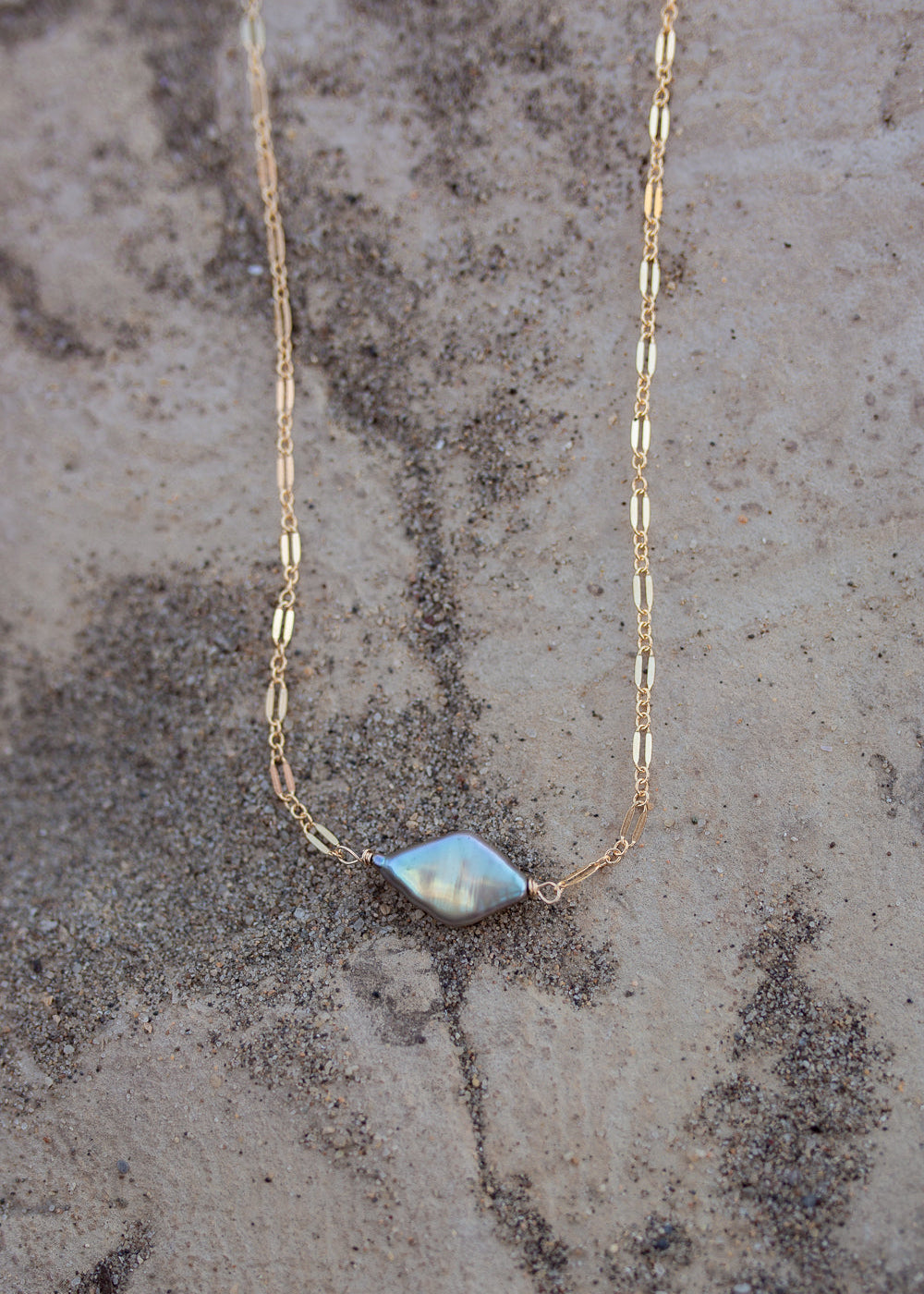 Sparkly gold necklace with a diamond shaped sage green pearl in the middle